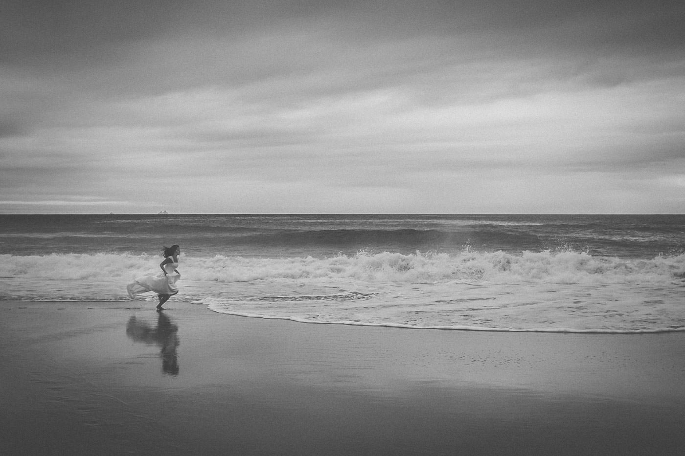 Braut rennt am Strand entlang, Schwarzweissbild mit Brandung im Hintergrund und ganz in der Ferne die Umrisse von Skellig Michael, After-Wedding-Session am Slea Head, Dingle, Co. Kerry, Irland