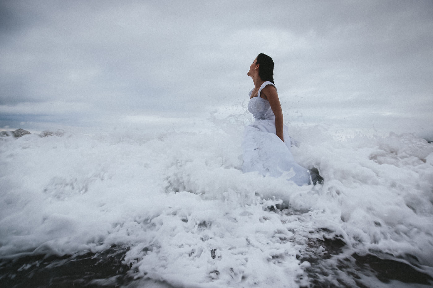 Bride in wedding dress struggling with a breaking wave in the Atlantic
