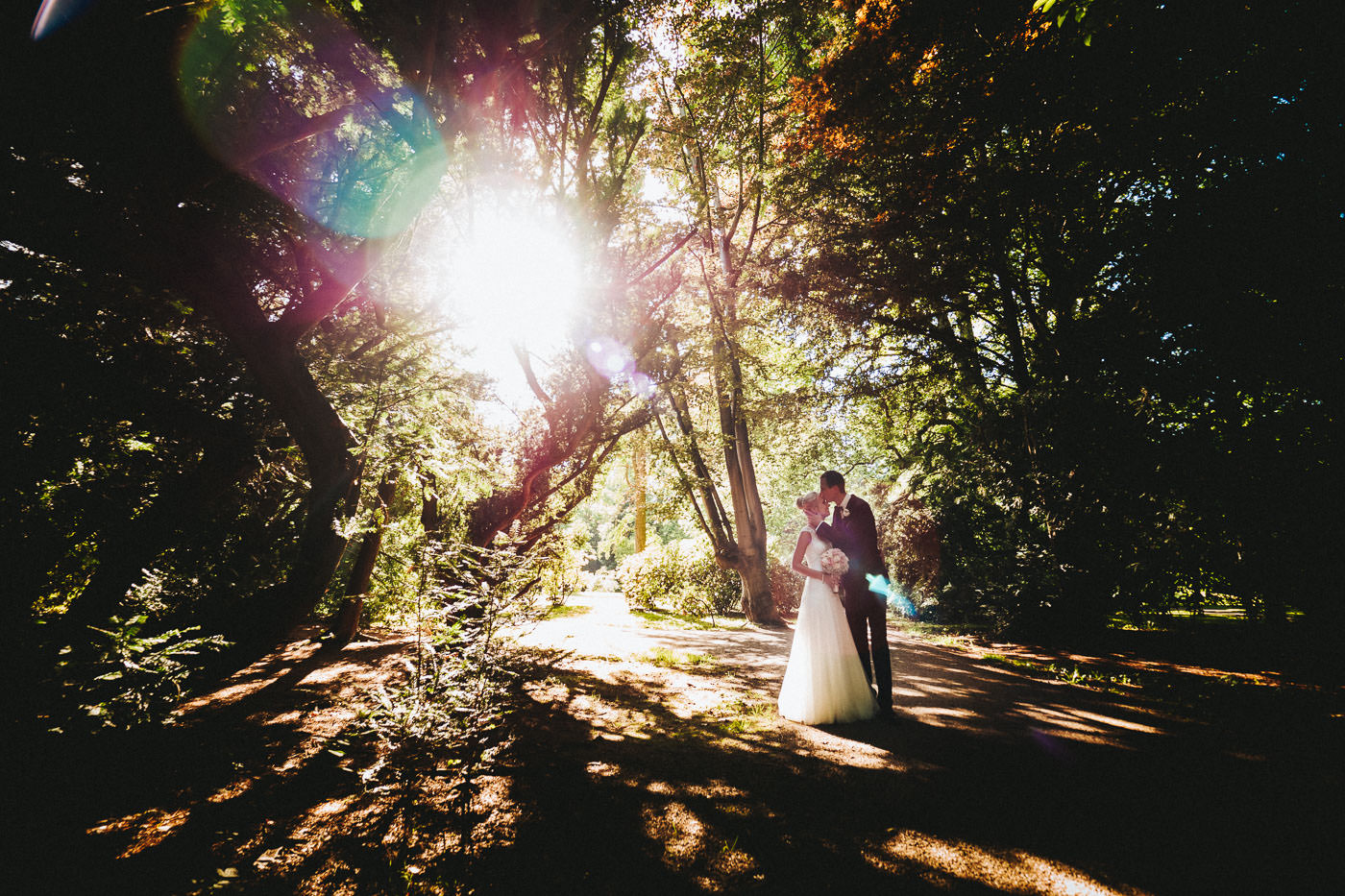 Bride and groom backlit under the trees in Bad Homburg spa park