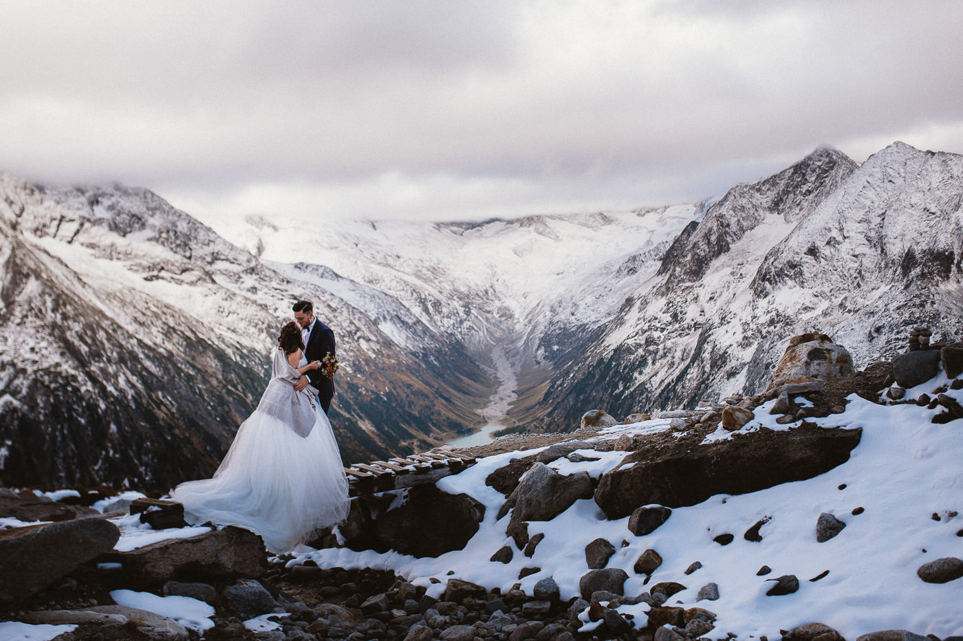 Bridal couple in the mountains, kissing on old wooden bridge with snow