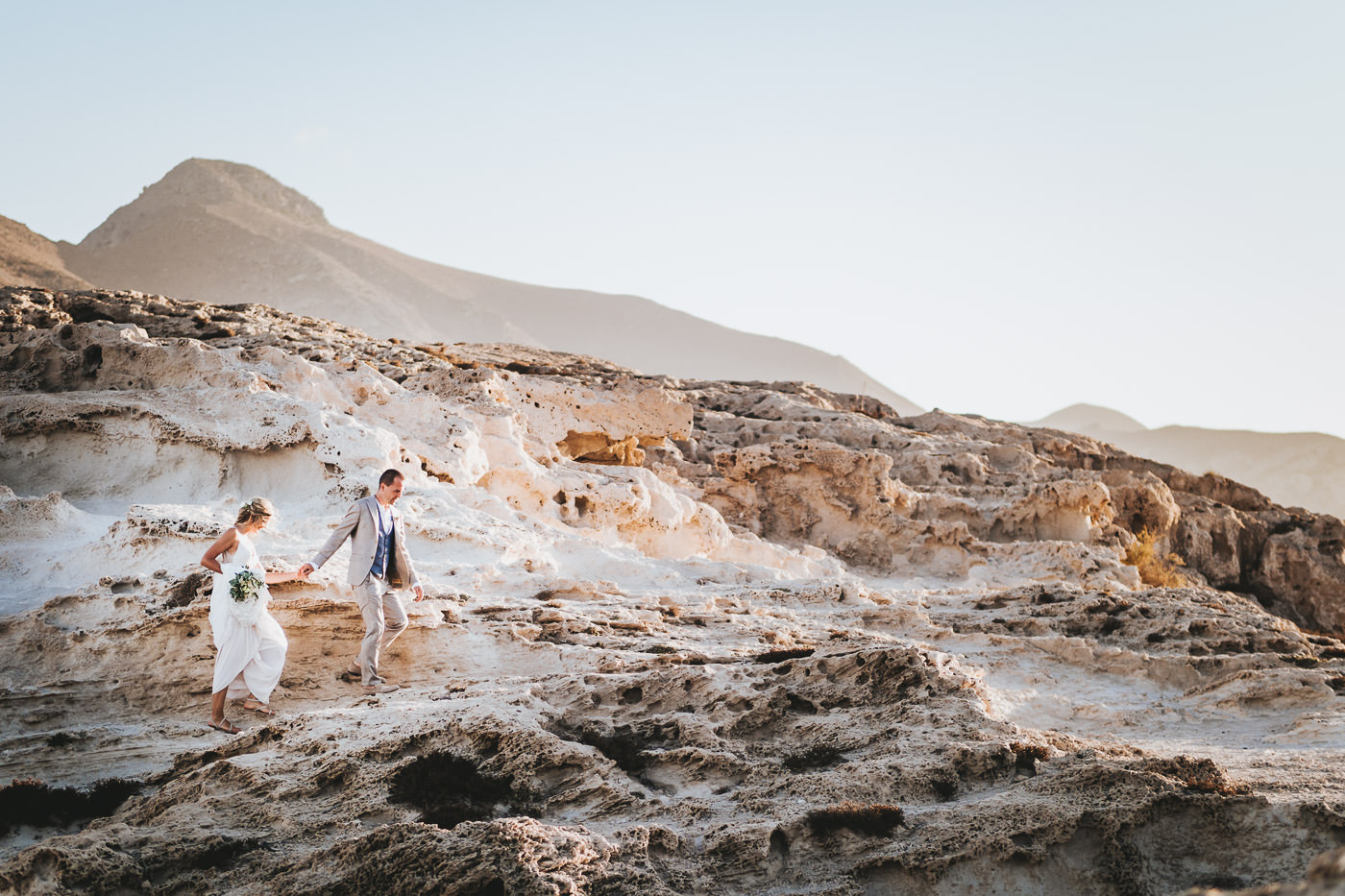Bridal couple walks in the evening sun over the rocky beach of Playa Los Escullos near Cabo de Gata in Andalusia, Spain - wedding photographer Andalusia, Brautrausch