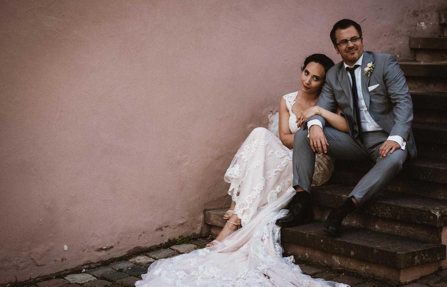 Bridal couple sitting relaxed on the stairs of Hornbach Abbey - train of the beautiful dress spread out on the floor
