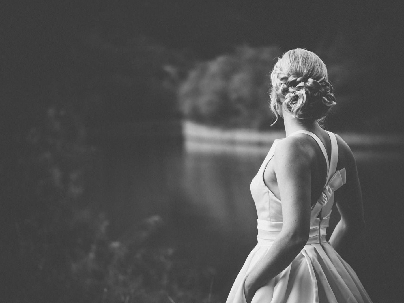 Bride with hands in the pockets of her wedding dress, looking at the river - wedding photos Schloss Saareck in black and white