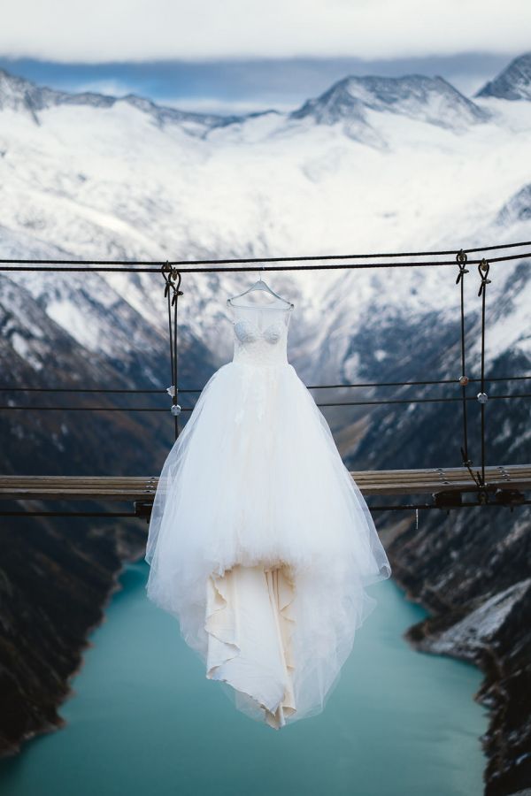 Brautkleid von Madam Burcu hängend an Hängebrücke mit blauem Stausee und schneebedeckten Zillertaler Alpen im Hintergrund