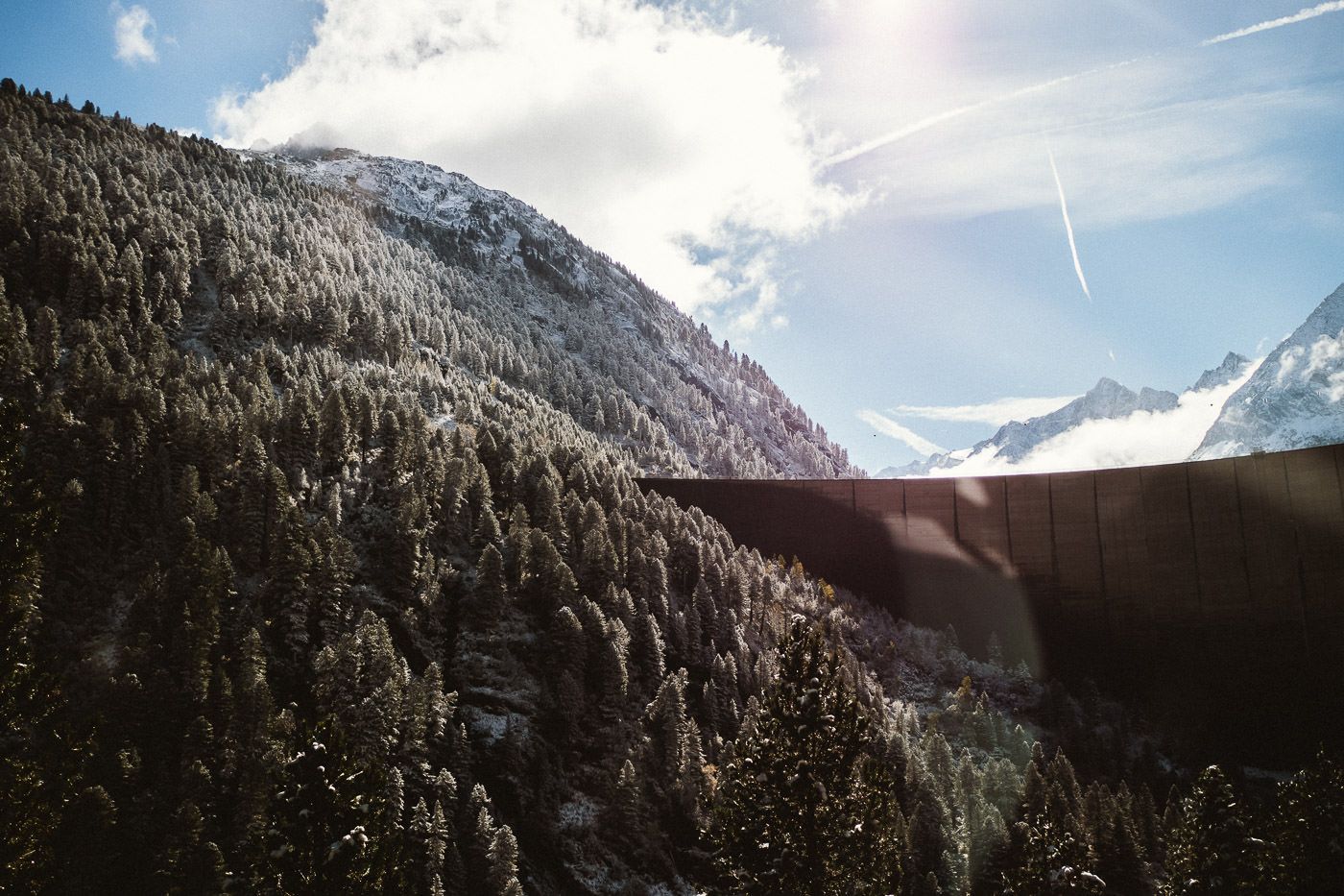 Staumauer des Schleggeisspeichers mit schneegezuckerten Bäumen im Gegenlicht