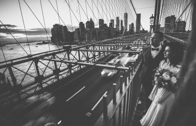 Hochzeitspaar auf der Brooklyn Bridge mit Blick über die Straße auf die Bucht mit Skyline von Manhattan im Hintergrund - Elopement in New York