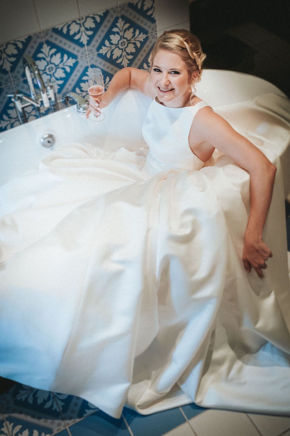 Braut im Brautkleid in schicker Badewanne mit Sektglas in der Hand