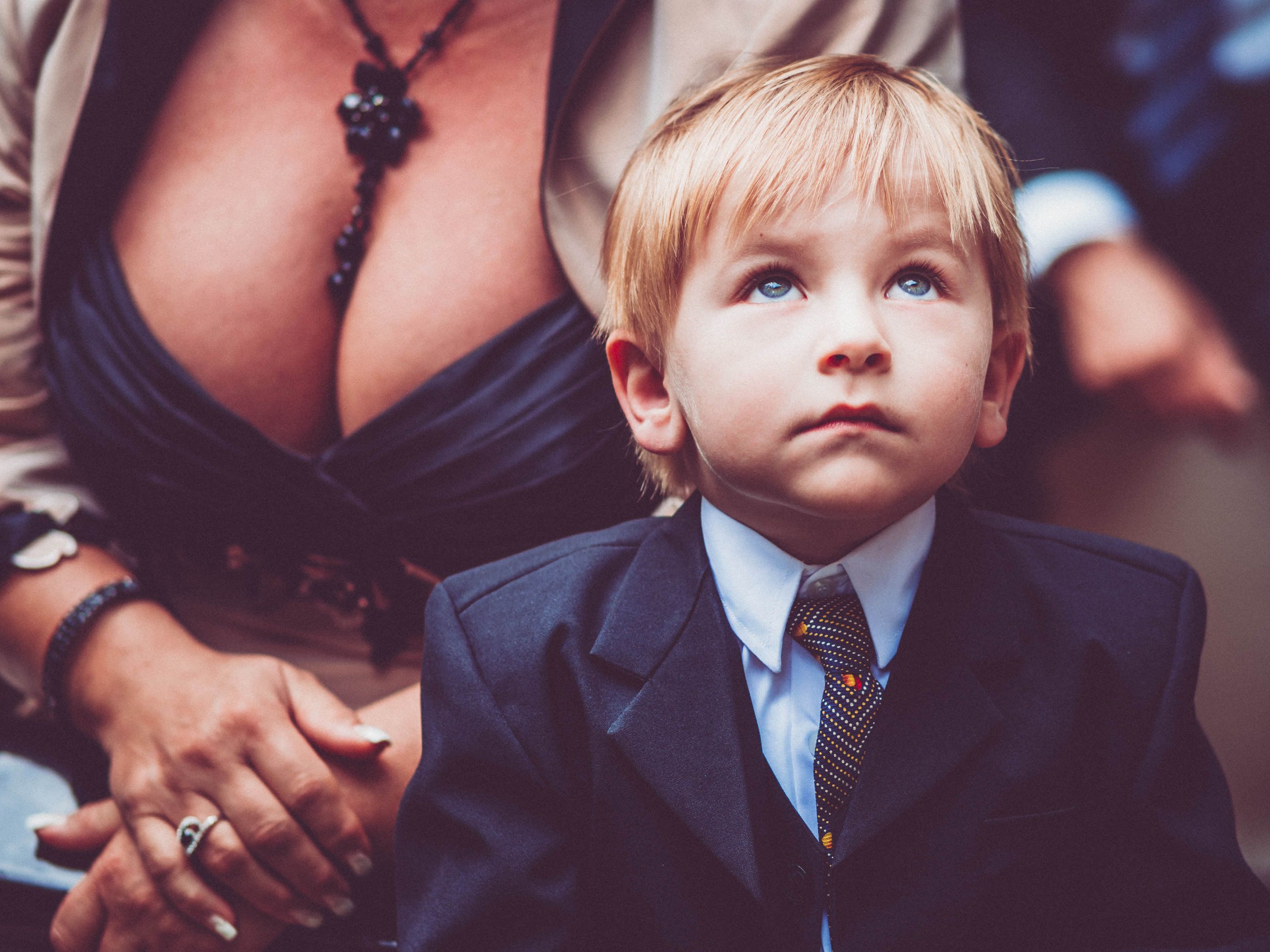 Kleiner Junge mit ernstem Blick und Hochzeitsgast mit tiefem Dekoltee im Hintergrund