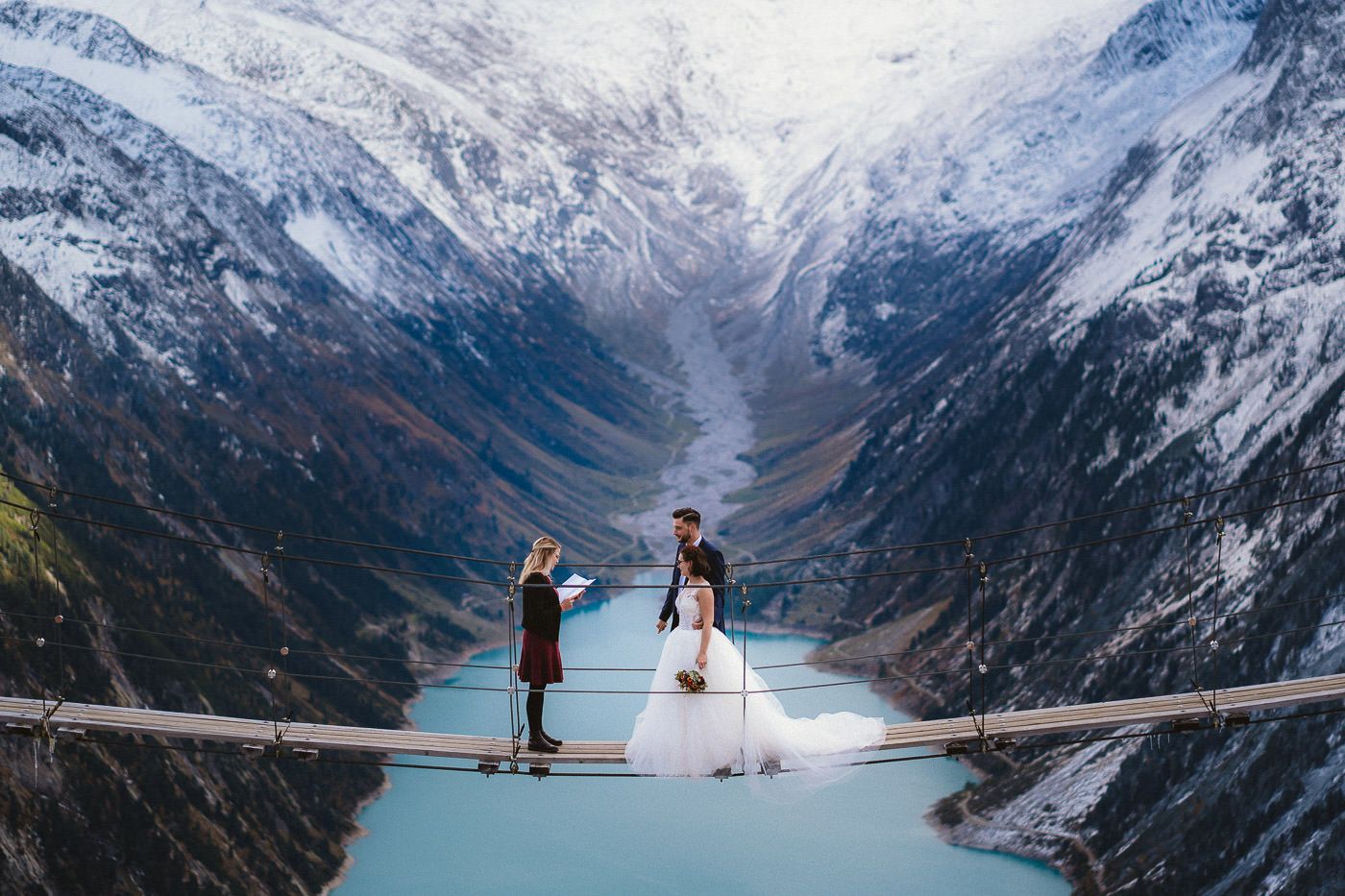 Brautpaar und Traurednerin bei freier Trauung vor spektakulärer Alpenkulisse - auf der Hängebrücke an der Olpererhütte im Zillertal, im Hintergrund ein Stausee und das Alpenpanorama