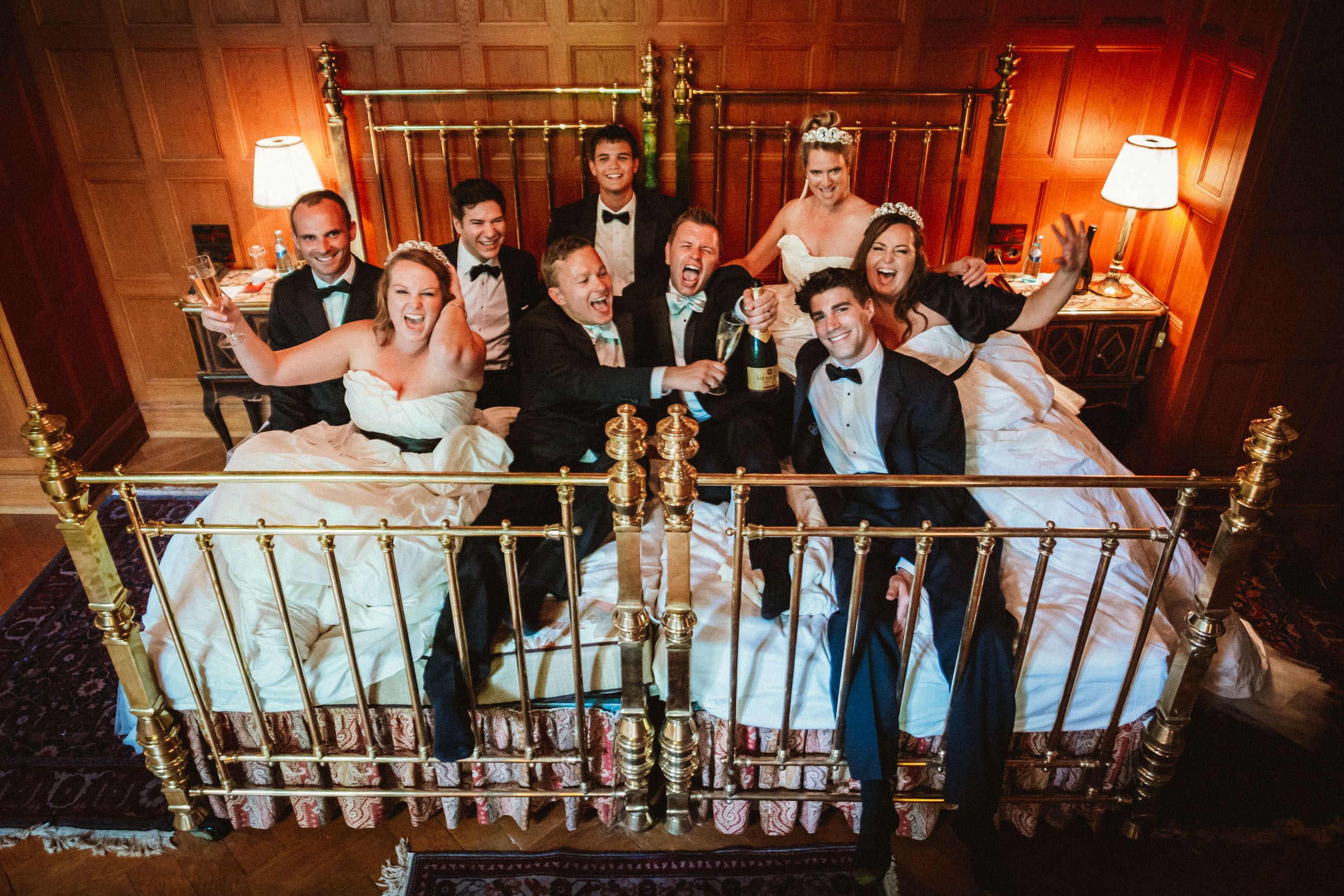 Schwules Hochzeitspaar mit Smoking und Fliege feiert im Bett mit Groomsmen und Bridesmaids in Brautkleidern - Partystimmung in der Suite von Schlosshotel Kronberg - Hochzeitsfotograf Taunus Brautrausch