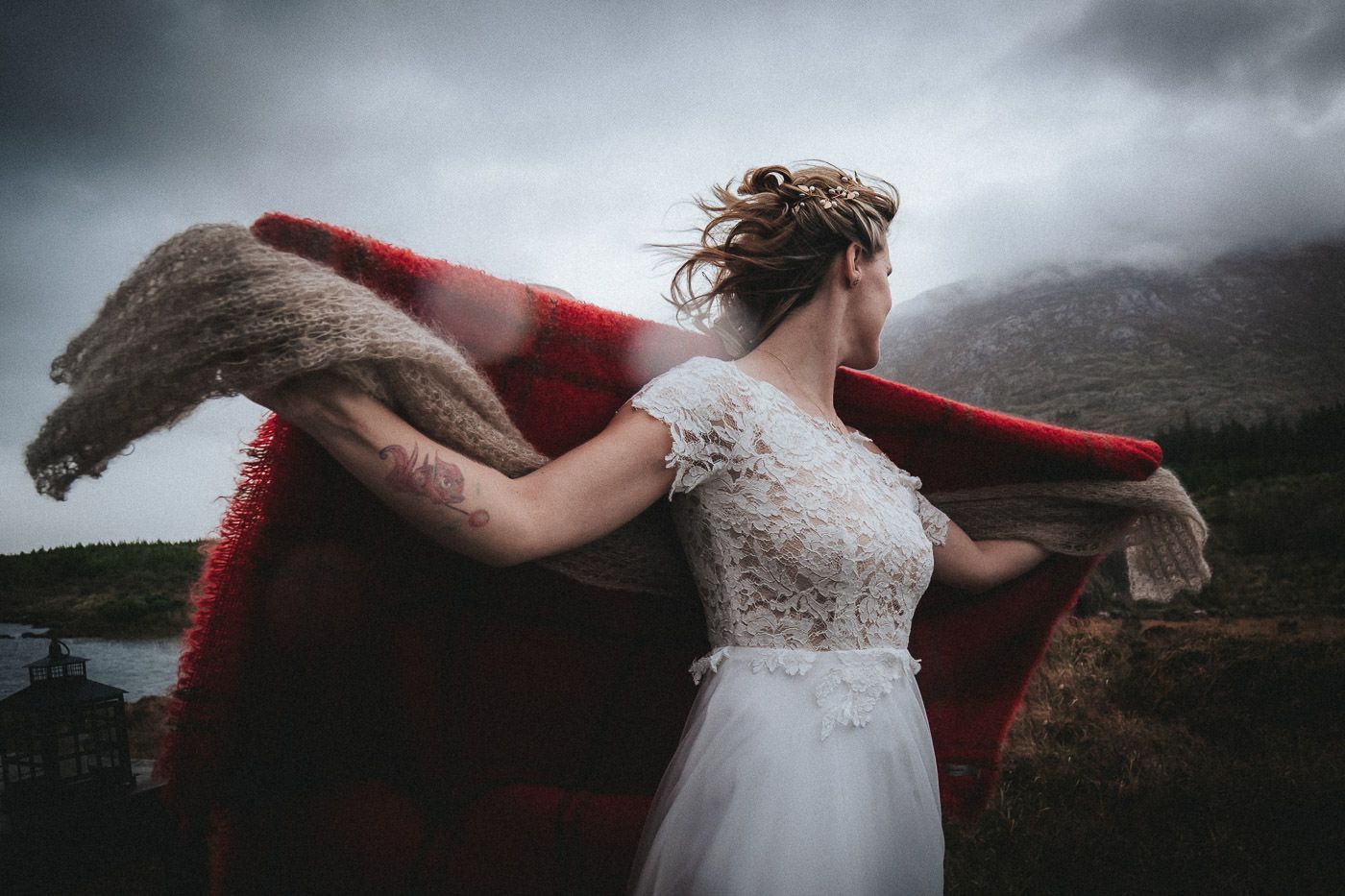 Düsterer Himmel über einer entschlossen wirkenden Braut im Boho-Kleid mit roter Wolldecke - Tiny Wedding in Irland