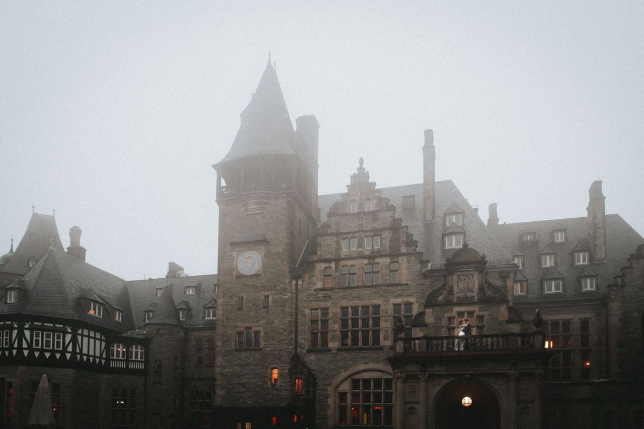 Front von Schlosshotel Kronberg im Herbstnebel, mit Brautpaar auf dem Balkon, aufgenommen im Rahmen einer internationalen Hochzeitsreportage - Hochzeitsfotograf Taunus Brautrausch