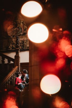 Küssendes Brautpaar auf der Treppe im Schlosshotel Kronberg, Braut im roten Kleid, Hochzeitsfoto einer Winterhochzeit, mit Reflektionen der Weihnachtsdekoration - Hochzeitsfotograf Taunus Brautrausch